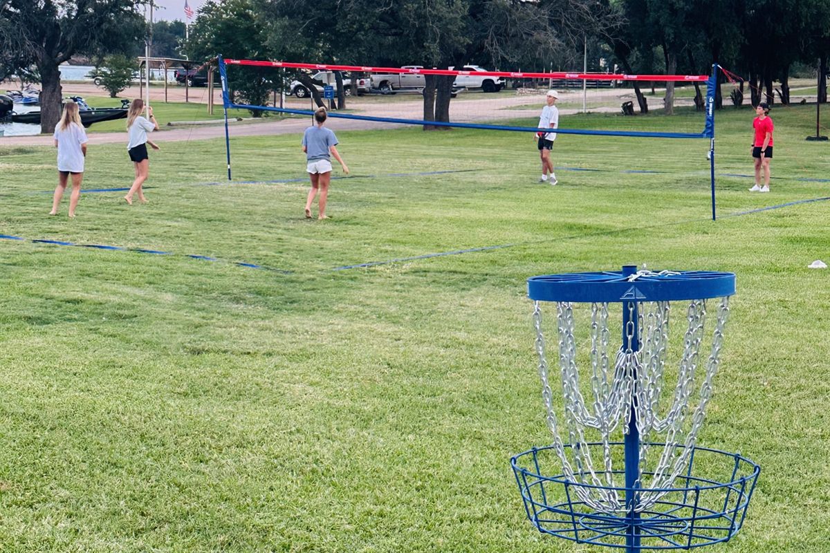 Guests playing volleyball on the lawn with a disc golf basket in foreground